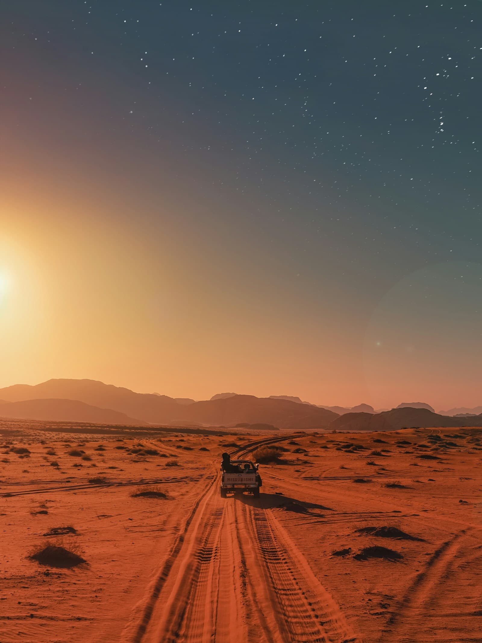 A jeep crossing the red sand of Wadi Rum at sunset